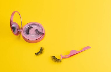 Sarı ışıklandırıcı arka planda pembe ayna setinde manyetik sahte kirpikler. Kirpik uzatma, kozmetik alet konsepti, güzellik tedavisi. Renk eğilimi