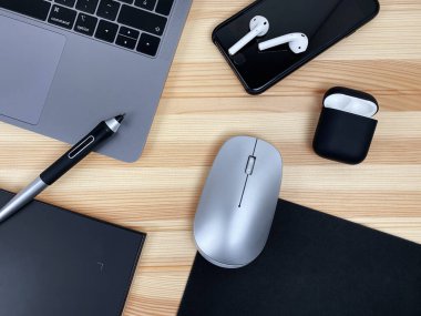 Gri laptop grafik tableti, akıllı telefon, fare, tahta masa arkasında kablosuz kulaklık. İş yatağı, minimalist tasarım, akıllı çalışma teknolojisi. 