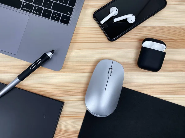 Gri laptop grafik tableti, akıllı telefon, fare, tahta masa arkasında kablosuz kulaklık. İş yatağı, minimalist tasarım, akıllı çalışma teknolojisi. 