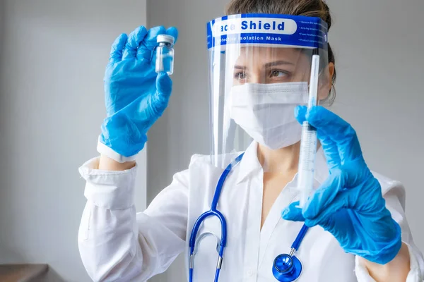 Doctor in mask and face shield holding vaccine vial and syringe. Vaccine development concept. Health care, medical equipment, researching