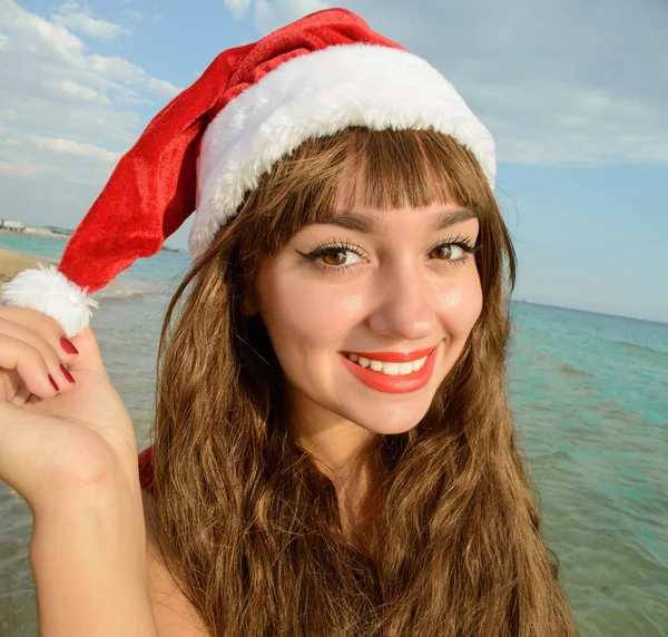 Gelukkig en mooi meisje santa claus op het strand. — Stockfoto