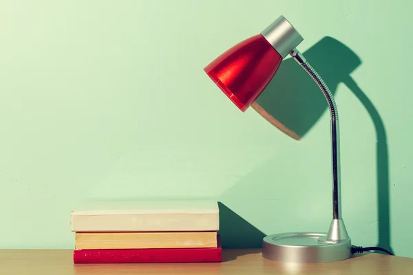 Livros e lâmpada vermelha na mesa de madeira . Imagem De Stock