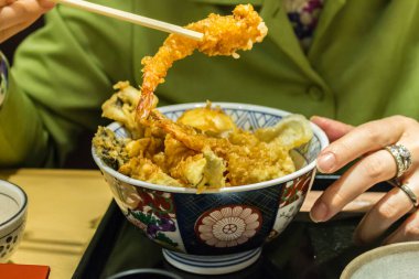 Japon Ishikawa Bölgesi, Kanazawa şehrinde, çeşitli balık ve sebze temposu kasesinin üzerinde yemek çubukları tarafından tutulan karides temposu..