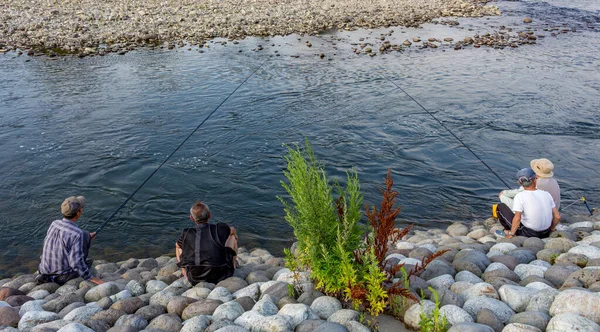 Men fishing on the stone riverbank of the Saigawa River, in summer, Kanazawa, Japan.