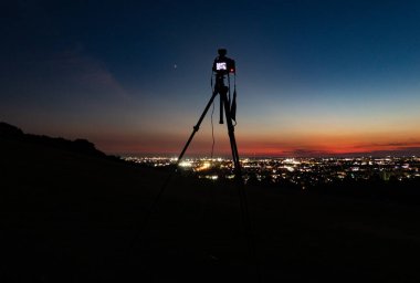 Günbatımından hemen sonra şehrin ışıklarını gösteren tripoddaki dijital SLR kameranın gece görüşü, arka kamera ekranı görünür. Kanazawa, Japonya.