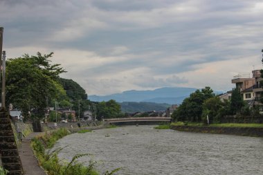 Asanogawa nehri ve köprüsünün uzak dağlarla manzarası. Kanazawa, Ishikawa Bölgesi, Japonya.