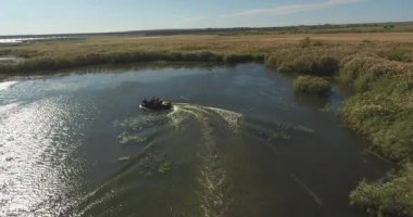Hava görüntüsü. Motorlu tekne kuru sazlıklar arasında sonbahar nehri boyunca hızla yüzer.