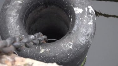Nehir limanındaki demir bir zincir üzerinde suyun arka planına karşı büyük, katı kauçuk kiriş çamurluğu.