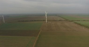 Hava görüntüsü. İnsansız hava aracı, çiftçilerin yeşil ve siyah tarlalarında bulunan rüzgar türbinlerine hızla yaklaşıyor. Manzara üzerinde sabah sisi