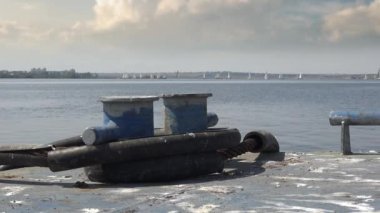 Demir bir rıhtımda demirli kalınlar ufukta spor yatları olan açık deniz ve nehrin arka planına karşı.