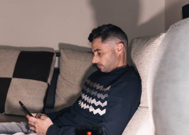 Softadaki cep telefonuna bakan kişi kanepedeki cep telefonuna bakıyor.