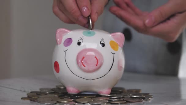 Das Sparschweingeschäft steht auf einem Haufen Münzen. Eine Hand steckt eine Münze in ein Lifestyle-Sparschwein auf gelbem Hintergrund. Geld zu sparen ist eine Investition in die Zukunft. Bankeninvestitionen. — Stockvideo