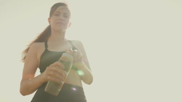 Dívka pije vodu z láhve v záři slunce. Žena má žízeň po útěku — Stock video