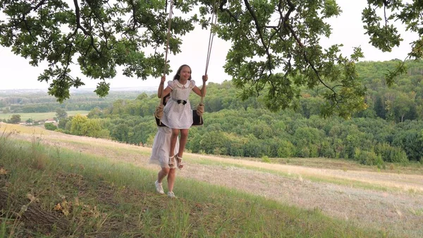 Moeder schudt het meisje op een schommel. Een kind met zijn moeder voor een wandeling in het park op een vrije dag. Teamwork. Gezinsleven — Stockfoto