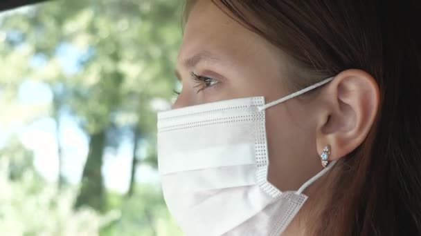 Ein schönes Mädchen fährt Auto und setzt sich eine Maske auf, um die Menschen um ihn herum nicht mit Covid-19 zu infizieren. Schutz vor Infektionen und Grippe. Nahaufnahme — Stockvideo
