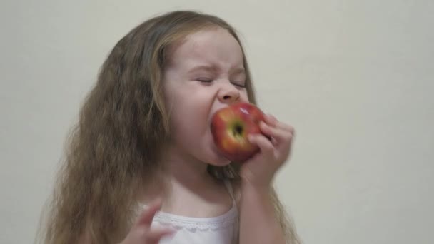 A little girl bites a red apple and chews. Healthy diet for children. Vitamin fruit. Taste of childhood. Close-up. The child eats delicious food. Food for a good intestinal tract — Stock Video