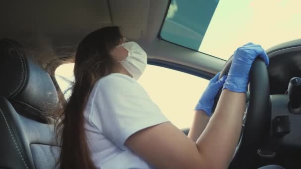Uma mulher está dirigindo um carro com uma máscara médica e luvas azuis. A rapariga dança e canta. Covid-19. Pandemia — Vídeo de Stock