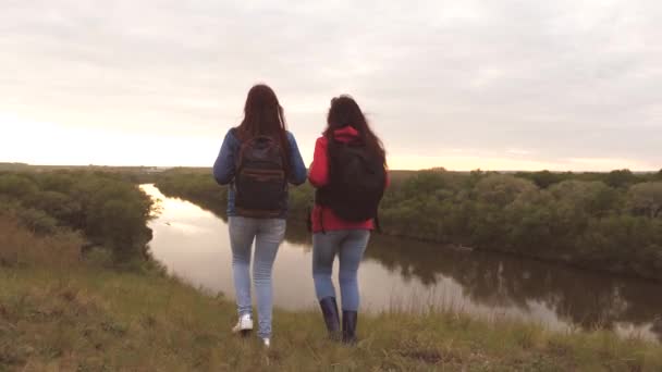 Flickvänner reser med ryggsäckar vid floden. Glada flickor turister letar efter äventyr. Lagarbete. Helg på motionsvandring bland kvinnor. Vila på naturen. Terrängforskning — Stockvideo