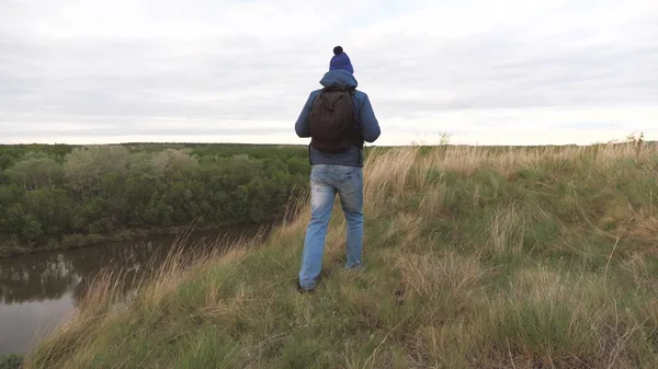 Een man reist met een rugzak op een berg bij de rivier. De man is op zoek naar avontuur. Een weekend op een sportieve wandeling alleen. Rust uit in de natuur. Toeristische verkenning van het gebied — Stockfoto