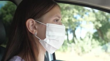 Güzel bir kız arabayla gider ve maske takar. Böylece etrafındaki insanlara Covid-19 bulaştırmaz. Enfeksiyon ve gribe karşı koruma. Yakın plan.