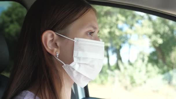 Een mooi meisje rijdt in een auto en zet een masker op om de mensen om hem heen niet te besmetten met Covid-19. Bescherming tegen infectie en griep. Close-up — Stockvideo