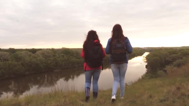 As namoradas viajam com mochilas junto ao rio. Meninas alegres turistas estão à procura de aventura. Trabalho de equipa. Fim de semana em uma caminhada esportiva entre as mulheres. Descanse na natureza. Investigação sobre o terreno — Vídeo de Stock