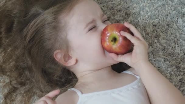 Une petite fille mord une pomme rouge et mâche. Une alimentation saine pour les enfants. Fruits vitaminés. Goût d'enfance. Gros plan. L'enfant mange de délicieux aliments. Nourriture pour un bon tractus intestinal — Video