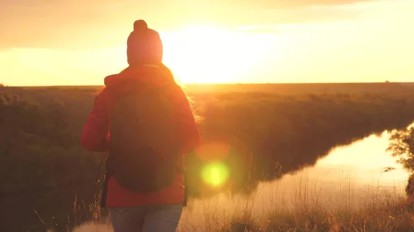 Mädchen Reisende in den Strahlen der Sonnenuntergangssonne mit einem Rucksack. Junge Touristinnen gehen auf einem hohen Berg und begegnen dem Sonnenaufgang. Abenteuerlust bei der Selbstfindung. Forschungsergebnisse verschiedener — Stockfoto