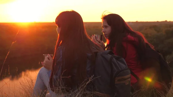 Viajantes do sexo feminino sentam-se no alto da montanha e bebem chá em uma caneca olhando para o pôr do sol. Conquistar novos lugares juntos. Fim de semana ativo. Mulheres livres turistas estão à procura de aventura na vida — Fotografia de Stock