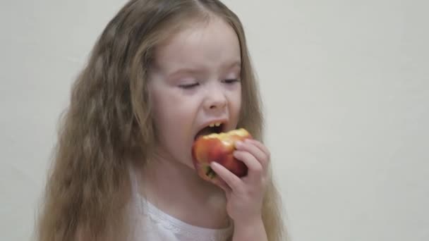 En liten flicka biter ett rött äpple och tuggar. Hälsosam kost för barn. Vitaminfrukt. Smak av barndom. Närbild. Barnet äter utsökt mat. Mat för en bra tarmkanal — Stockvideo