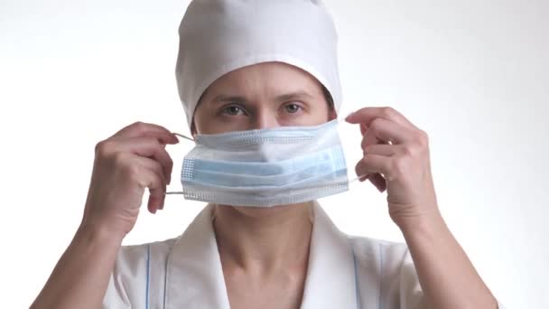 L'operatore sanitario indossa una maschera e sorride. Ritratto ravvicinato del personale medico. Donna in maschera protettiva.Isolata su sfondo bianco. Assistenza sanitaria e concetto medico. Primo piano — Video Stock