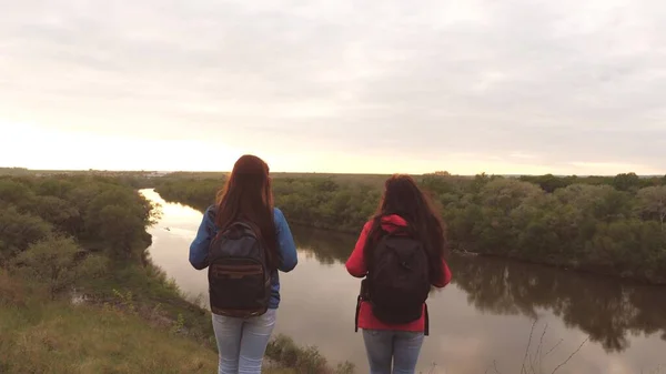 Vriendinnen reizen met rugzakken bij de rivier. Vrolijke meisjes toeristen zijn op zoek naar avontuur. Teamwork. Weekend op een sportieve wandeling onder vrouwen. Rust uit in de natuur. Terreinonderzoek — Stockfoto