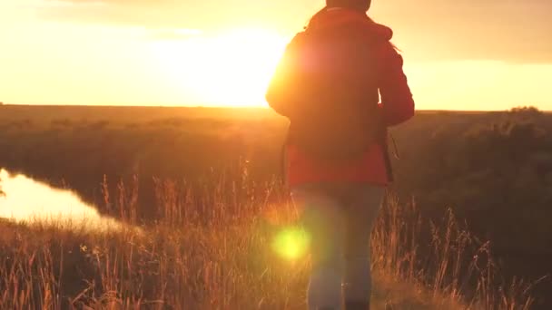 Girl traveler in the rays of the sunset sun with a backpack. Young woman tourist walks on a high mountain meeting the sunrise. Thirst for adventure in finding yourself. Research findings of various — Stock Video