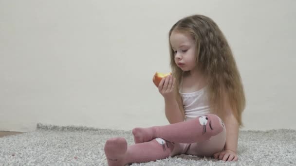 Une petite fille mord une pomme rouge et mâche. Une alimentation saine pour les enfants. Fruits vitaminés. Goût d'enfance. L'enfant mange de délicieux aliments. Nourriture pour un bon tractus intestinal — Video