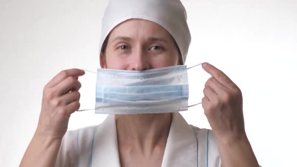 De zorgverlener doet een masker op en glimlacht. Medisch personeel close-up portret. Vrouw met beschermende masker.Geïsoleerd op witte achtergrond. Gezondheidszorg en medisch concept. Close-up — Stockvideo