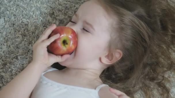 En liten flicka biter ett rött äpple och tuggar. Hälsosam kost för barn. Vitaminfrukt. Smak av barndom. Närbild. Barnet äter utsökt mat. Mat för en bra tarmkanal — Stockvideo