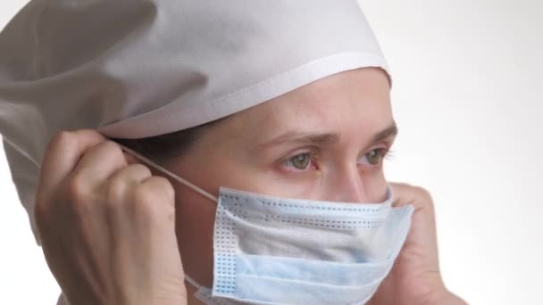 Zdravotnický pracovník si nasadí masku a usměje se. Zblízka portrét zdravotnického personálu. Žena v ochranné masce. Izolované na bílém pozadí. Zdravotní péče a lékařská koncepce. Detailní záběr — Stock video