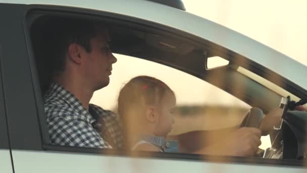 Papai ensina sua filhinha a girar o volante enquanto está sentado em seu carro no assento dos motoristas. pai viaja com crianças de carro. O condutor e o miúdo estão a conduzir. família feliz e conceito de infância — Vídeo de Stock