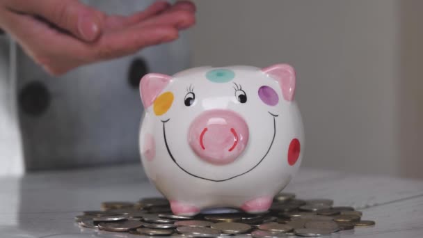 Das Sparschweingeschäft steht auf einem Haufen Münzen. Eine Hand steckt eine Münze in ein Lifestyle-Sparschwein auf gelbem Hintergrund. Geld zu sparen ist eine Investition in die Zukunft. Bankeninvestitionen. — Stockvideo
