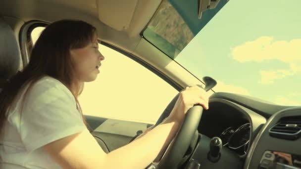 Jovem mulher dirigindo em um carro ou campista viaja pelo campo. A rapariga está sozinha no transporte. Canta a melodia da canção, as vibrações das férias de verão — Vídeo de Stock