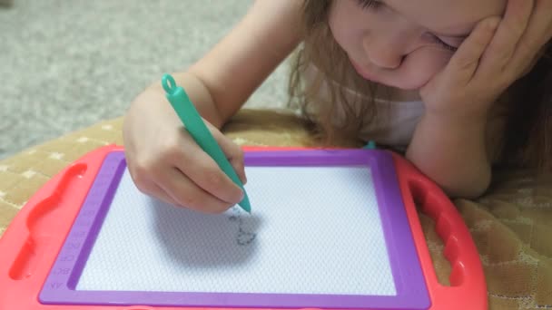 Klein meisje tekent een tekening en glimlacht. Een gelukkig kind doet waar hij van houdt. Kinderhobby. Hij ontwikkelt motoriek. Leuke spelletjes thuis — Stockvideo