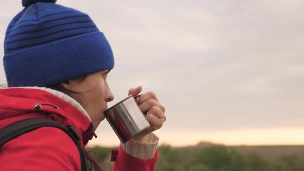 Een jonge meidenreiziger zit alleen op de berg en drinkt warme thee van een mok. Vrouw toerist met een rugzak rustend op een weekendwandeling. Winderig weer in de natuur. De man is op vakantie. Eenzaamheid — Stockvideo