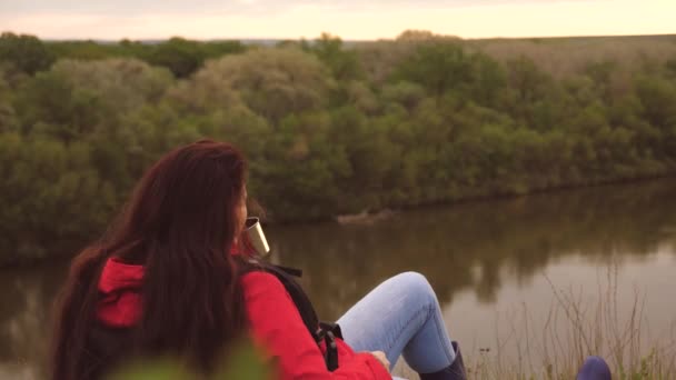 Une jeune voyageuse s'assoit seule sur la montagne et boit le thé chaud d'une tasse. Touriste femme avec un sac à dos reposant sur une randonnée de week-end. Temps venteux dans la nature. Il est en vacances. La solitude — Video