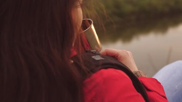 Een jonge meidenreiziger zit alleen op de berg en drinkt warme thee van een mok. Vrouw toerist met een rugzak rustend op een weekendwandeling. Winderig weer in de natuur. De man is op vakantie. Eenzaamheid — Stockvideo