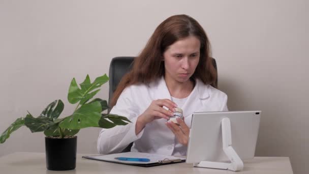 Online overleg met een tandarts via een tablet. Vrouwelijke orthodontist houdt pleistertanden vast en bijt in haar hand. Een kaakbehandeling in een gespecialiseerd dokterskantoor. Een gezonde en mooie glimlach op de — Stockvideo