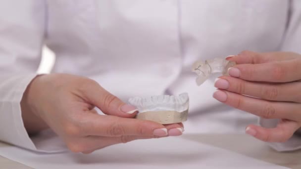 Женщина-ортодонт держит в руке пластину для коррекции зубов и прикуса. Чтобы положить тарелку на гипсовые белые зубы. Лечение челюстей в кабинете специалиста. Крупный план — стоковое видео