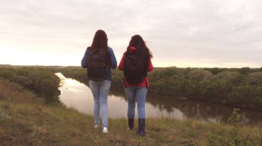 Kız arkadaşlar sırt çantalarıyla nehir kıyısına seyahat ederler. Neşeli kızlar macera arayan turistler. Takım çalışması. Kadınlar arasında hafta sonu spor yürüyüşü. Doğada dinlen. Toprak araştırması