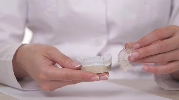 Bir kadın ortodontist elinde diş düzeltme ve tıkanıklığı için bir tabak tutuyor. Plastik beyaz dişlere plaka takmak için. Uzman bir doktor muayenehanesinde çene tedavisi. Sağlıklı ve güzel