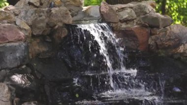 Saf temiz su doğadaki taşlardan yavaşça akar. Uçan spreyli küçük şelale