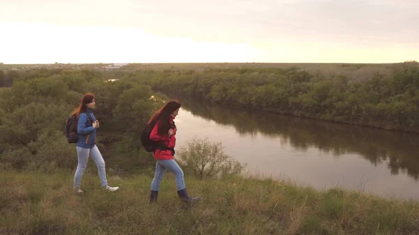 Vrouwelijke reizigers met rugzakken lopen langs een hoge berg en glimlachen. Vriendinnen wandeltocht. Levensavonturen van vrouwen in de natuur. Teamwork. Familieweekend bij de stromende rivier — Stockfoto